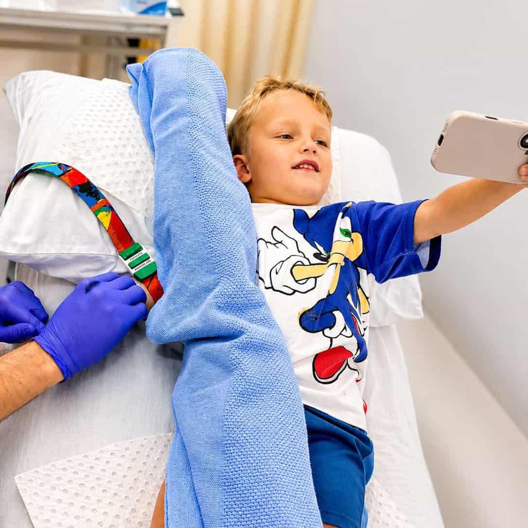 Boy distracted with a phone while a tourniquet is applied for a blood test at the BRAVE Clinic, Shire Family Medical, Sutherland