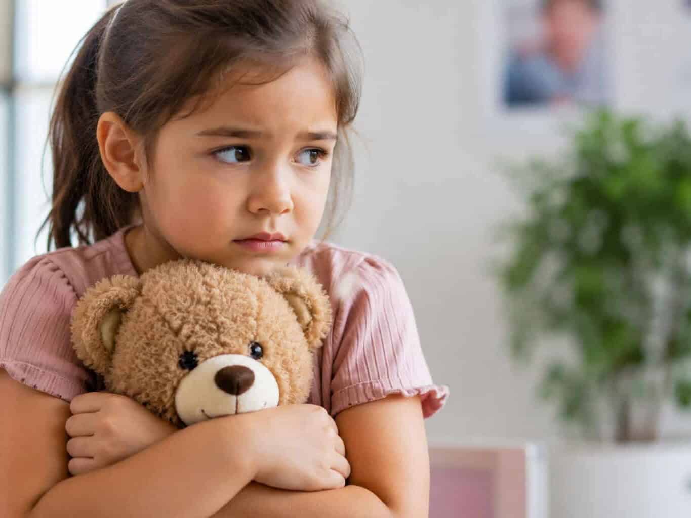 Young girl hugging her teddy bear with a worried expression while waiting at the GP, illustrating how to help prepare children for vaccinations.