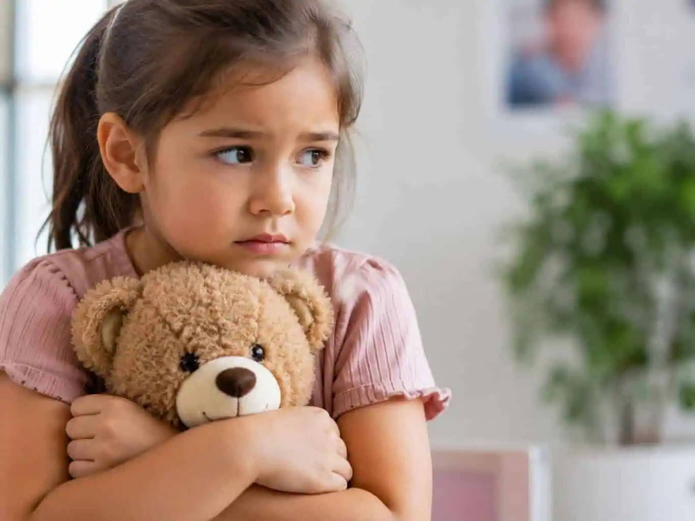 Young girl hugging her teddy bear with a worried expression while waiting at the GP, illustrating how to help prepare children for vaccinations.