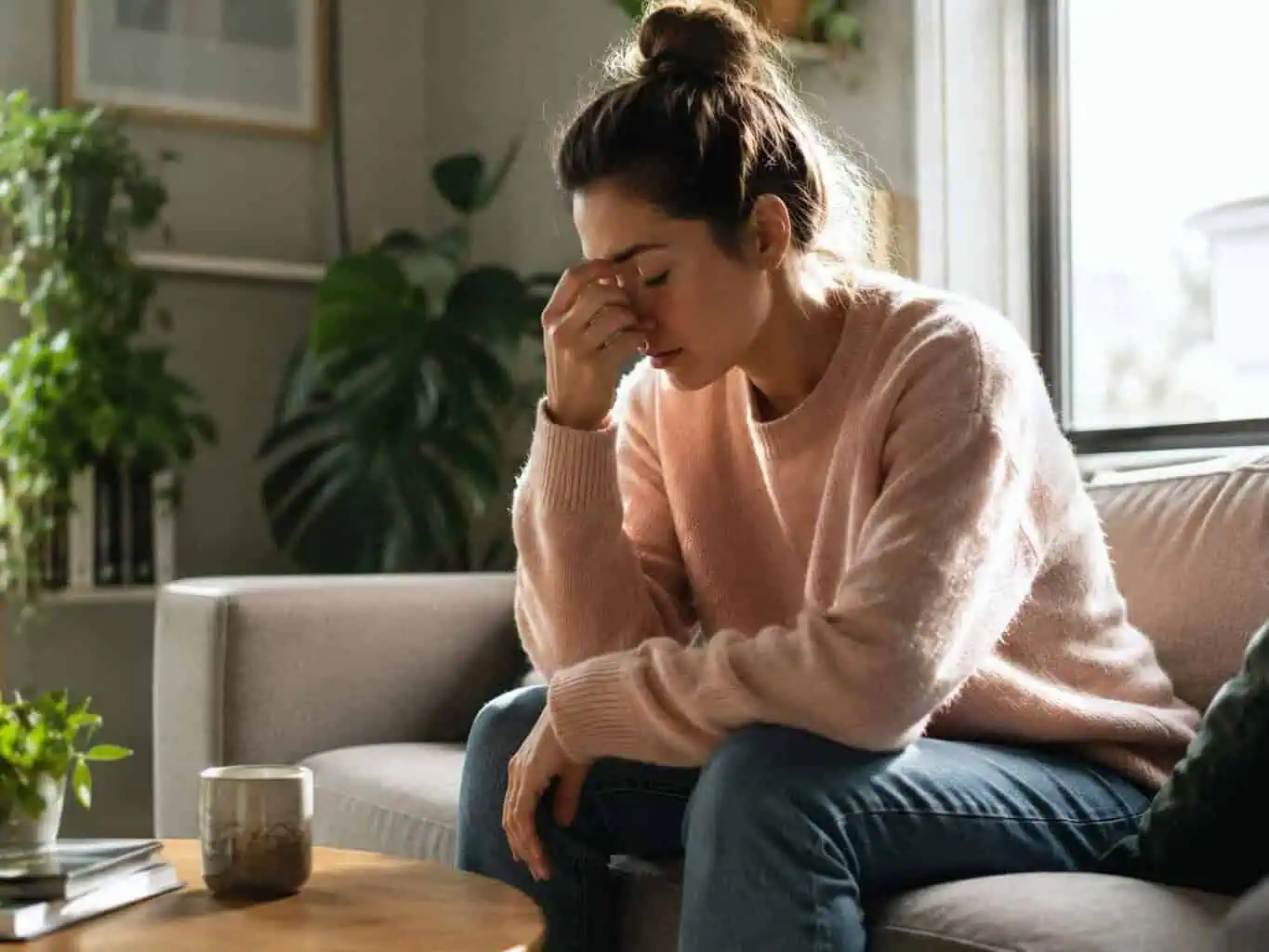 Woman sitting on the couch pinching the bridge of her nose, looking exhausted and stressed, illustrating ongoing fatigue that may need a GP check.