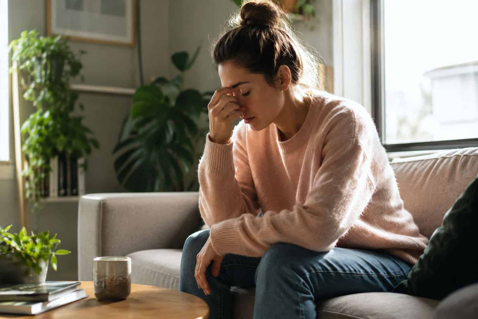 Woman sitting on the couch pinching the bridge of her nose, looking exhausted and stressed, illustrating ongoing fatigue that may need a GP check.